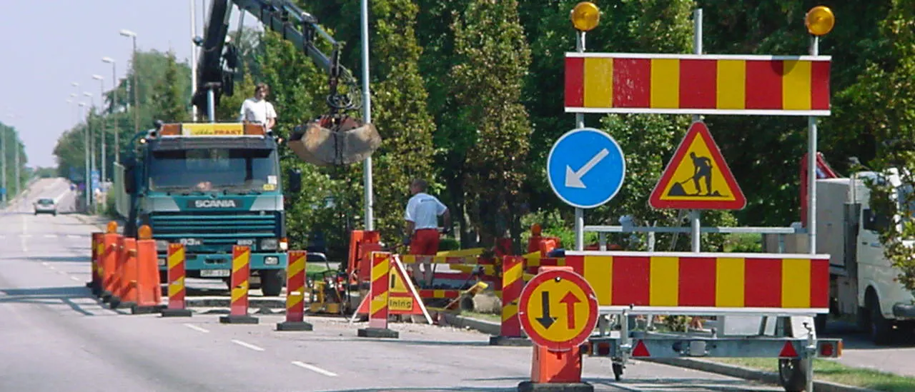 Vägarbete med lastbil, markeringsskärmar, varningsmärke och påbudsmärke som leder trafiken förbi arbetsplatsen